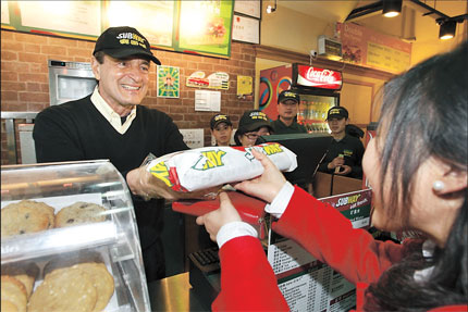 Frederick A. Deluca (left), president and founder of sandwich chain Subway, passes a sandwich he made to a customer in an outlet in Shanghai during his visit to the city yesterday. Subway plans to have 500 outlets on China's mainland within five years. [Shanghai Daily]