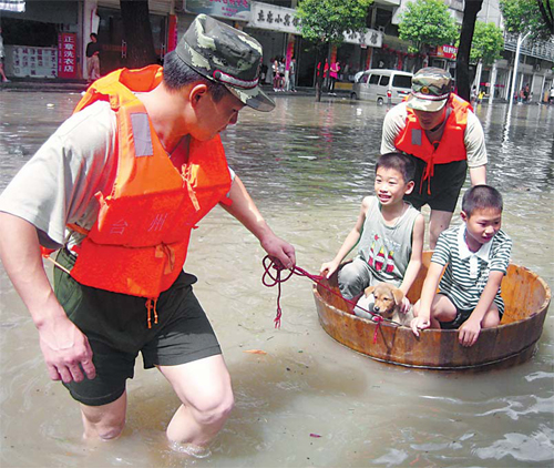Rescue workers help two boys and a dog to safety from a flooded street on Tuesday in Taizhou city in East China’s Zhejiang province. [China Daily] 