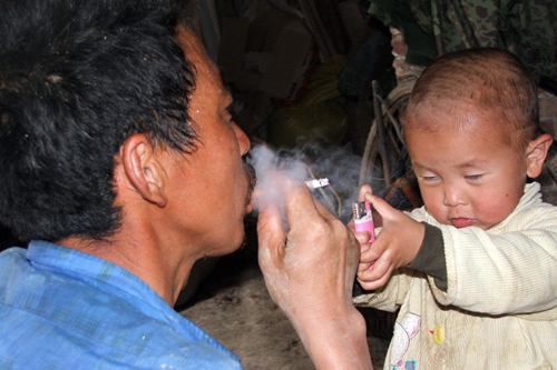 A boy lights a cigarette for his father on May 26 in Shaoyang, Hunan province. [China Daily]
