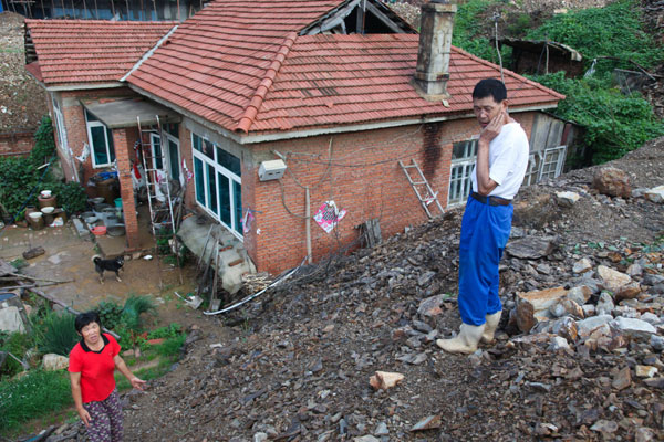 Yu Zhixu (right), a villager from Lushun, Liaoning province, stands at the mound of stones next to his home in July in this file photo. Because of a disagreement about the compensation a real estate developer offered Yu to demolish his home to make way for urbanization, the developer blocked his access to the outside by piling sand and stones 3 meters high next to his home. [Provided to China Daily] 