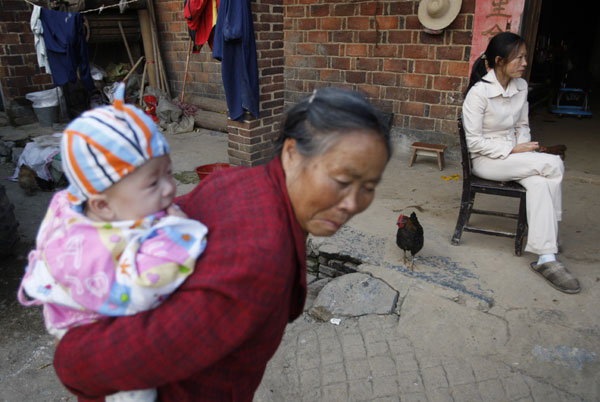 Yang Deying sits in her courtyard in Nanta village, Hunan province, while her mother-in-law carries one of her twins. Yang, 32, returned to the willage two years ago to get married.