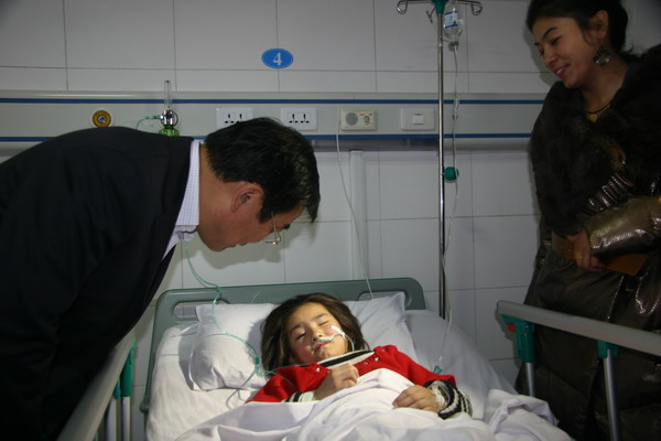 A severely injured victim of the stampede at Aksu No 5 Primary School is visited in hospital by Huang Sanping, Party secretary of Aksu prefecture, on Monday. The accident may have started when a child slipped on the stairs. [Photo/Xinhua]