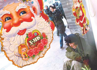 A homeless man shelters from the cold in front of a shop, adorned with Christmas decorations, in Dongdan, Beijing after refusing help from a State-run social assistance center.