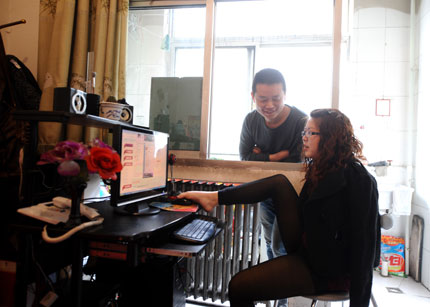 Luo Fengzhi controls a mouse with her foot to manage her online store at home in Taiyuan City, Shanxi Province, as her husband, Xu Jin, looks on. 