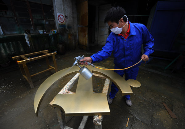 A man spray paints a newly-made Party emblem in a factory in Anqing city, East China's Anhui province, June 28, 2011. 