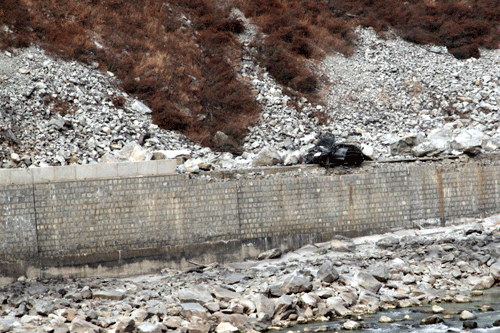 This section of the old road from Dujiangyan to Wenchuan was buried by falling rocks. In the foreground is the wreck of a black car crushed by boulders. 