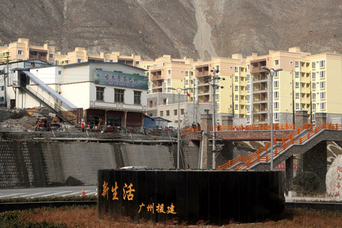 A new village, built with the help of the Guangdong Provincial Government, takes shape at the foot of a mountain. The sign on the monument in the village square says “New Life”.