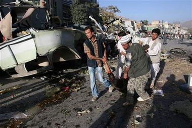 幾名阿富汗人從爆炸地點抬出一具政府軍士兵屍體。