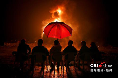 2007年7月12日，英國貝爾法斯特安特裏姆郡，人們坐在雨中觀看巨大的篝火。