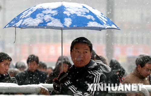 1月27日，一名旅客手持雨伞冒雪进郑州火车站候车。 当天，河南省黄河以南大部分地区普降中雪，局部地区大到暴雪，造成郑州火车站6趟列车紧急停运。