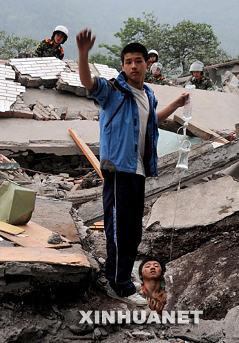 　5月13日，在四川省北川县地震灾区，一名北川中学学生在武警官兵帮助下救助被压在瓦砾堆中的同学。