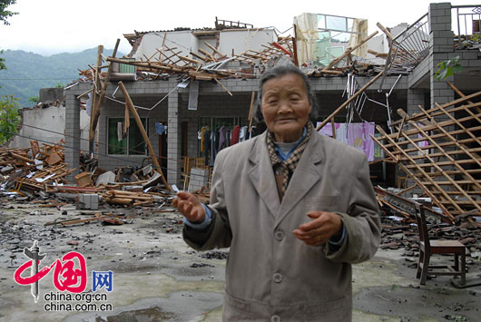 2008年5月14日，四川彭州市宝山村80多岁的老人，站在自家倒塌的房屋前。 罗小韵/摄