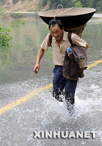 5月17日，一村民背着炊具正涉水紧急转移。