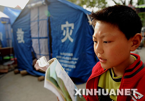 5月18日，9岁小学生刘严冰在帐篷前朗读课文。汶川地震后，四川省青川县的中小学全部停课。乔庄小学学生刘严冰请求父亲在废墟中找出课本，帐篷前又响起了读书声。