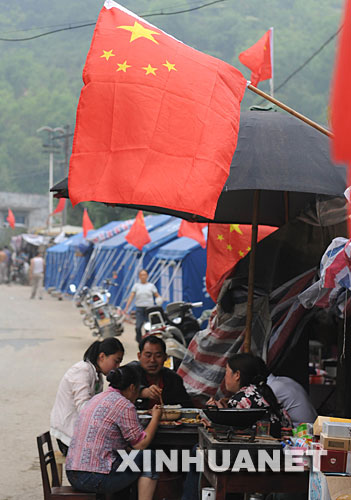 在四川省北部的青川县,几名灾区群众在挂有国旗的帐篷旁吃午饭
