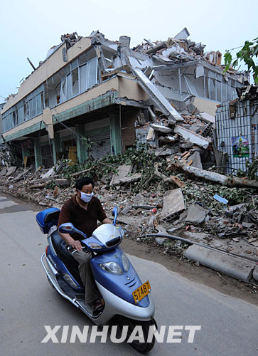 5月25日，市民骑摩托车从震后废墟旁驶过。