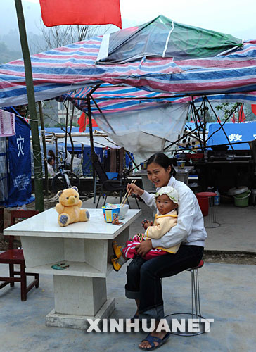 5月25日，一位年轻的母亲在给孩子喂饭。     目前，地震重灾区青川县已逐步恢复通电、通水，一些商店和商铺开始营业。居住在帐篷里的灾区群众冷静面对灾后生活，准备重建家园。