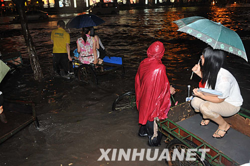 6月2日，几名行人利用三轮车通过被雨水浸泡着的广州街道。