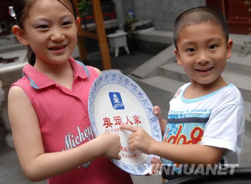  7月11日，居住在北京南官房衚同39號的朱鎔靖（左）和朱宥伊小朋友展示“奧運人家”瓷盤。當天，居住在北京什剎海南官房衚同39號的朱寶華一家成為首家被頒發“奧運人家”瓷盤標誌的家庭。據悉，北京共評選出“奧運人家”598戶，可提供726間客房，能一次接待1000多名中外觀眾和遊客。