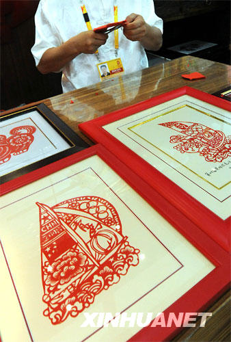 在青岛奥运村中国民俗展的展区内，艺人在现场制作剪纸作品