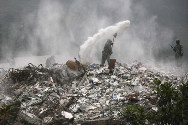 2008年5月24日，四川省北川县北川高中遭地震袭击倒塌，士兵们正在向碎石中喷洒消毒剂。
