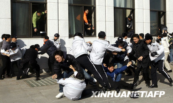  1月3日，在南韓首都首爾，警察（穿灰白色上衣者）阻止反對黨成員爬窗進入國會。南韓主要反對黨民主黨議員自2008年12月26日起佔據了國會大會議廳內的議長座位，以阻止執政的大國家黨單方面通過一系列有爭議法案。
