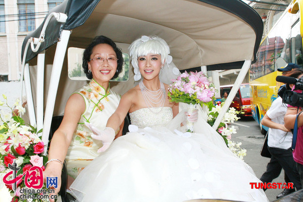 身穿纯白色拖地婚纱的新娘子张茜在母亲的陪伴下乘坐白色马车往教堂