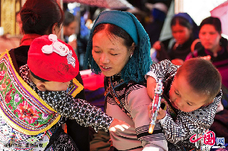 集市上，一个母亲背上的孩子被另外一个孩子手里的玩具吸引。　中国网图片库/郑跃芳 摄