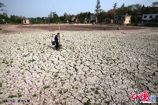 2013年3月28日，四川眉山市仁寿县农旺乡黄坭村村民挑水经过已龟裂的蓄水塘。中国网图片库 姚永亮摄