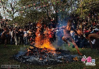 2013年3月14日，云南弥勒县，红万村祭火节，纹身蒙面的小伙子身上涂满了泥巴，纵情越过熊熊燃烧的篝火。中国网图片库 何东平摄