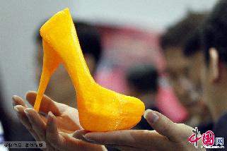 2013年4月25日，第六届中国留学人员南京国际交流与合作大会在南京国际博览中心举行，大会现场展示的一款由3D打印机打印出来的塑料高跟鞋让参观者大饱眼福。图为工作人员在展示3D打印机打印出来的高跟鞋。中国网图片库 董金林 摄