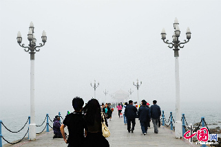 2013年5月23日，正值旅游旺季，可山东青岛栈桥略显冷清。当日温度急降，许多游客来不及更换衣物，在冷风中瑟瑟发抖。  中国网图片库  王海滨 摄影