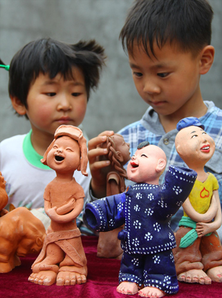 6月7日，两名小学生在欣赏民间艺人刘进潮的泥塑艺术作品。中国网图片库 张强/摄  