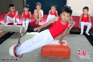 7月30日，在安徽省亳州市文帝东路亳州体操训练基地体操馆内，孩子们正在教练的指导下强化训练。图为小队员们在用自制的器械进行训练。中国网图片库 刘勤利摄