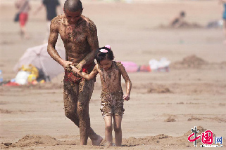 2013年8月11日，各地气温持高不下，阵阵热浪和紫外线考验着大家身心的耐受能力，但人们总是想出各种妙招来抵御高热的侵袭。图为一位爸爸和女儿全身涂满沙子，以防止高热和紫外线的侵害。   中国网图片库 王海滨摄影