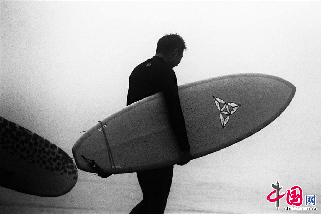 2013年8月11日，青岛持续的高温天气，使海边成了热点旅游地区。当日下午，石老人风景区游人如潮，进入秋季以来，沿海地区“高烧”不退，闷热天气仍未缓解，游客海边扎堆下水，避暑纳凉场面壮观。图为手持冲浪板的男子走向大海。 中国网图片库  王海滨摄影