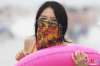 2013年8月11日，各地气温持高不下，阵阵热浪和紫外线考验着大家身心的耐受能力，但人们总是想出各种妙招来抵御高热的侵袭。图为为防止紫外线灼伤皮肤，一位下海冲浪的游客穿着泳衣、围起百变头巾。  中国网图片库 王海滨摄影