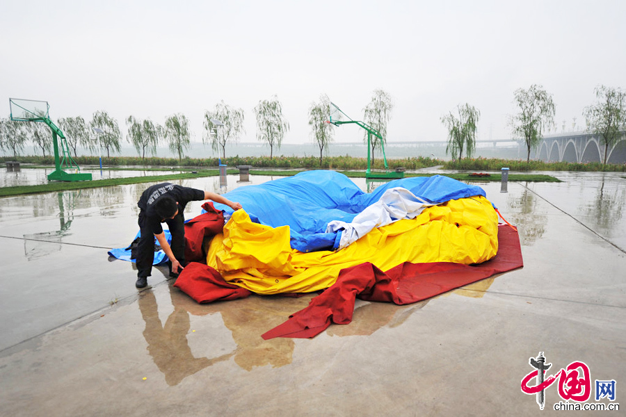  2013年9月04日，北京，瘪了气的大黄鸭被蓝色防雨布、红色雨毡遮住。9月3日深夜，大黄鸭到达北京园博园，并进行了充气试验。图为9月4日凌晨，大黄鸭到达北京园博园。凌晨四点，大黄鸭被用蓝色的防雨布遮盖起来。 图片来源：何笑颜/CFP