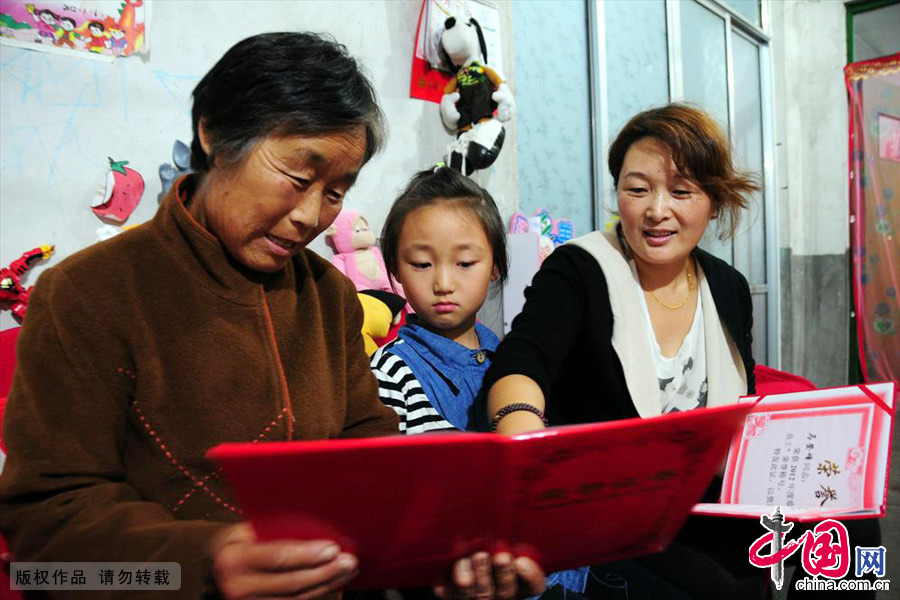 马登峰的母亲、爱人和女儿在看他获得的荣誉证书。母亲说登峰的爸爸干了一辈子农电工，村里人都夸，她希望他能和他爸爸一样，成为一个人人夸的人。中国网图片库 房德华/摄