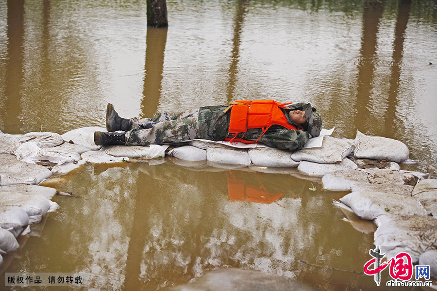 抗洪期间，一名身体疲惫的战士躺在洪水之间的沙袋上和衣而睡。