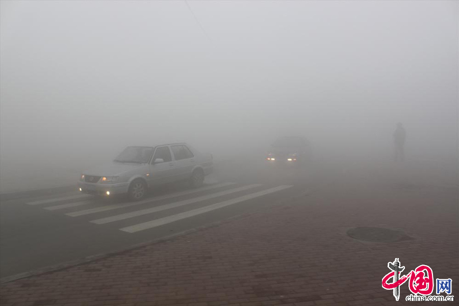 2013年10月21日，大霧能見度不足十米，行人過馬路小心翼翼，汽車行駛至路口彼此鳴笛判斷對方位置。中國網(wǎng)圖片庫 知言攝影