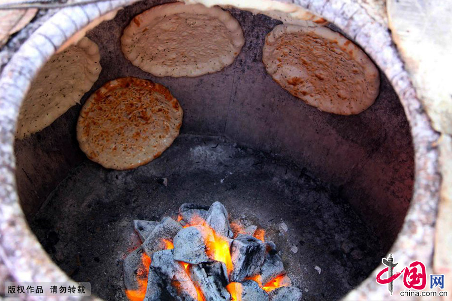 庫爾班只烤兩種哈密人愛吃的馕：蔥花馕，油馕。他的烤馕很受歡迎，烤馕的囊坑比一般的馕坑要大。中國網圖片庫 孫繼虎/攝
