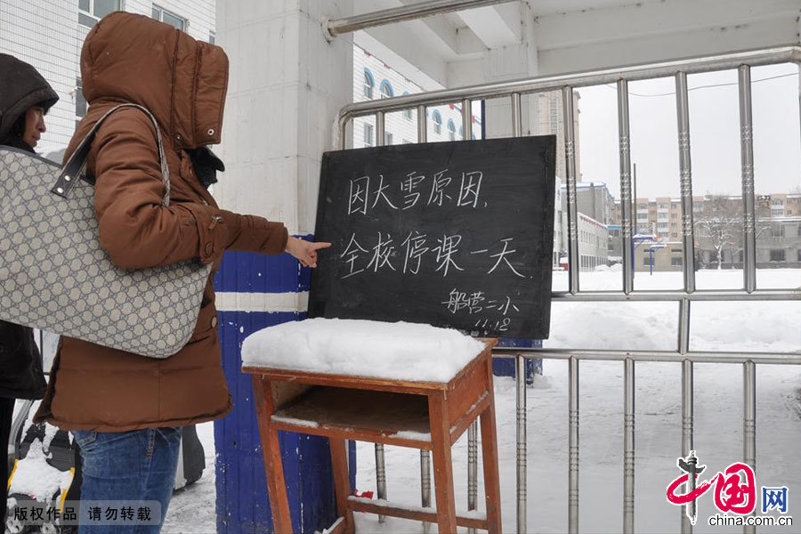 2013年11月18日，在吉林省吉林市船营区第二小学门前，家长带领孩子观看“降雪停课通知”。中国网图片库 王明铭