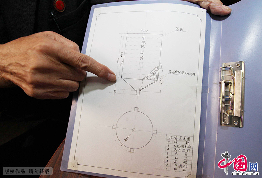  张金泰拿着图纸介绍整台过滤器的结构。从外观来看，这只是一个普通的纯净水塑料桶放置在铁架子上，但在塑料桶里面却“别有洞天”。中国网图片库 澎湃/摄 