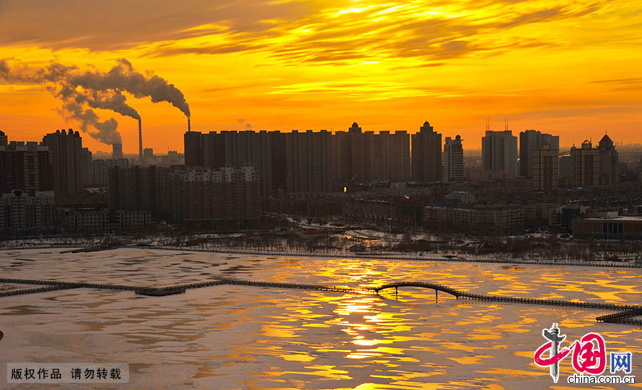  油城冬季的早晨，暖暖的橘黄色阳光洒在百湖之城的黎明湖上，淡淡的云雾缭绕在城市的上空，冬日暖阳、白雪、林立的高楼，构成一幅北方油城冬季风光图。中国网图片库 乔晓春/摄