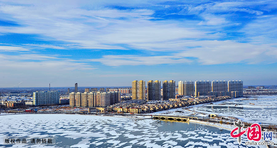  油城大庆的冬季已经来临，百湖之城被白雪覆盖，淡淡的云雾缭绕在城市的上空，蓝天白云下的湖面上白雪晶莹剔透，与远处的楼房相映成趣。中国网图片库 乔晓春/摄 