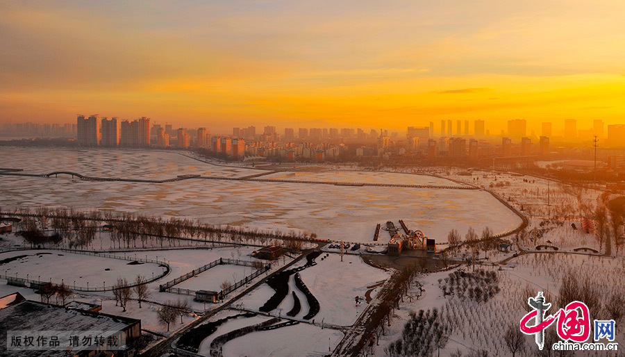  油城冬季的早晨，暖暖的橘黃色陽光灑在百湖之城的黎明湖上，淡淡的雲霧繚繞在城市的上空，冬日暖陽、白雪、林立的高樓，構成一幅北方油城冬季風光圖。中國網圖片庫 喬曉春/攝
