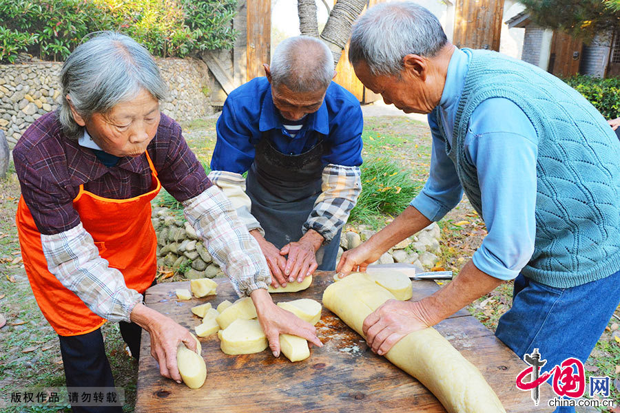  村民们将黄米果在木板上用力揉搓，使它成为一个圆筒状，最后，再用手把它稍微压扁一些，这样黄米果就算大功告成。中国网图片库 郑跃芳/摄
