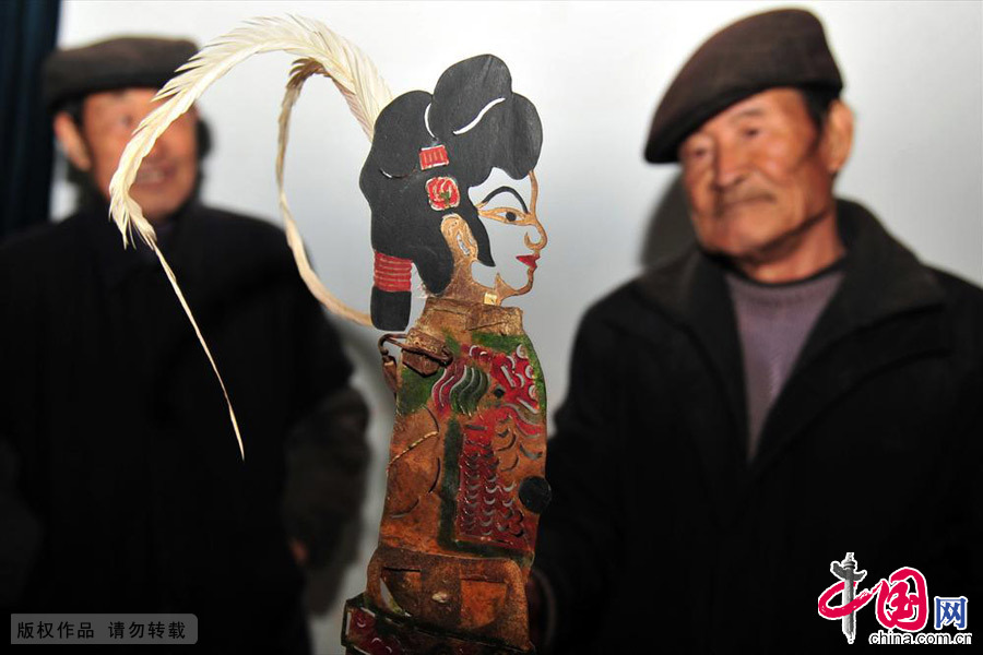 2013年12月11日，民间艺人向德根（右）在第二届皮影戏展演舞台的后台展示表演皮影戏的道具。中国网图片库 张国荣/摄
