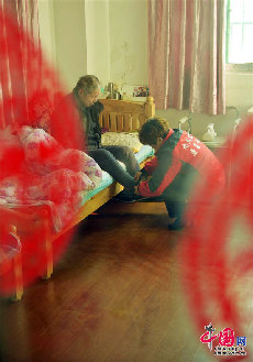 12月13日，刘彤在为一名老人穿鞋下床锻炼。(中国网图片库 封疆江摄影）  